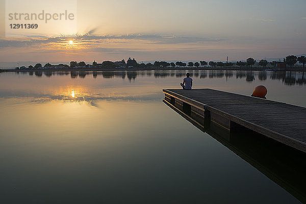 Relaxed girl on the floating platform on the lake at sunrise