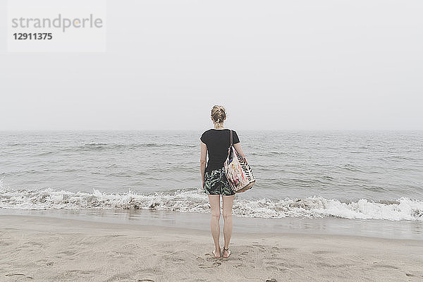 Back view of woman standing on the beach looking at distance