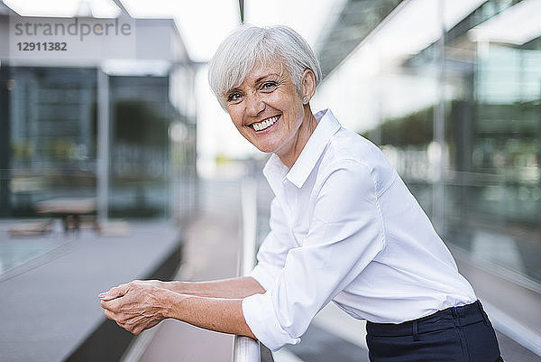Portrait of happy senior woman leaning on railing in the city