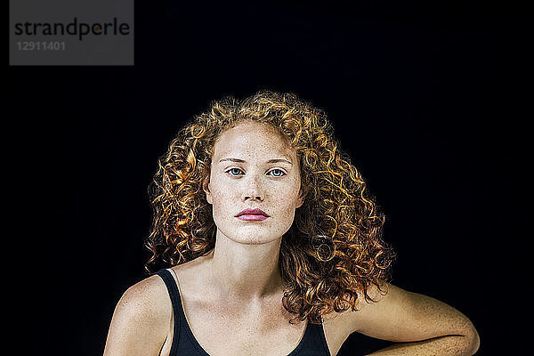 Portrait of freckled young woman with curly red hair in front of black background