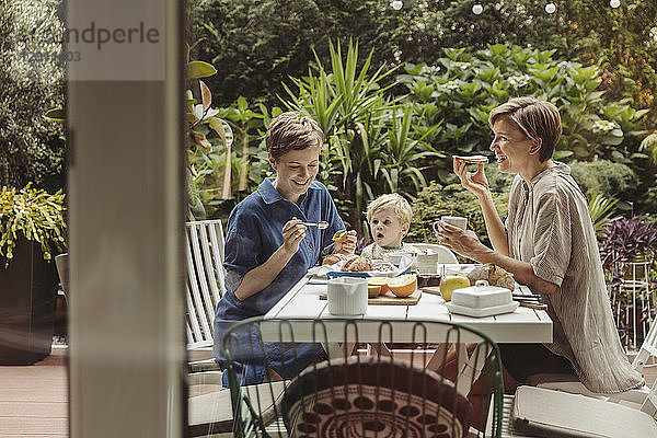 Two happy mothers at breakfast table outdoors with their child