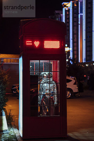Spaceman standing in a telephone box at night