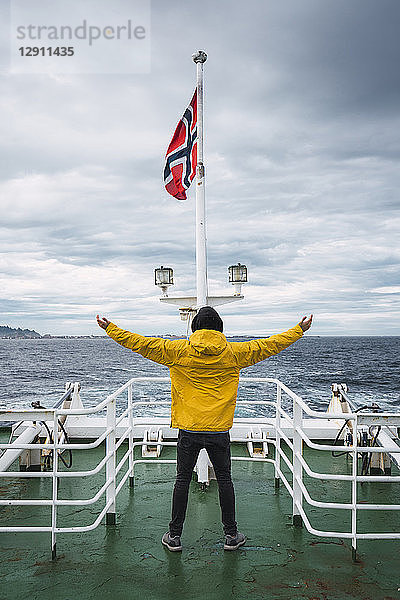 Norway  Senja island  rear view of man standing on ship deck with outstretched arms