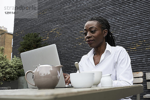 Portrait of smiling businesswoman sitting on terrace of a coffee shop working on laptop