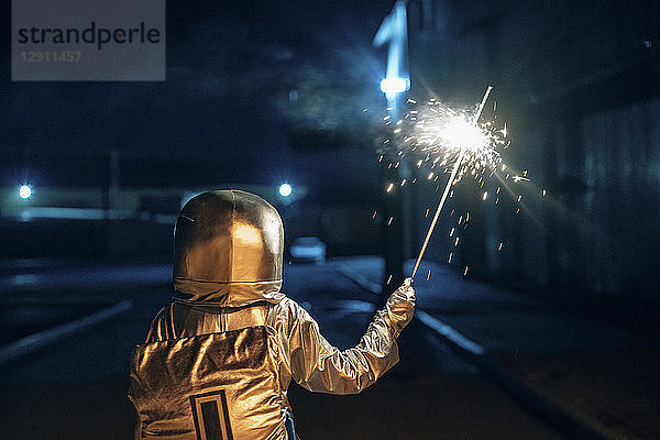 Rear view of spaceman standing outdoors at night holding sparkler