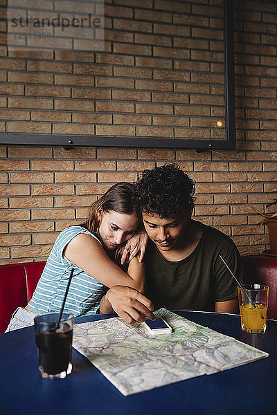 Affectionate young couple sitting at table in a cafe with map and cell phone