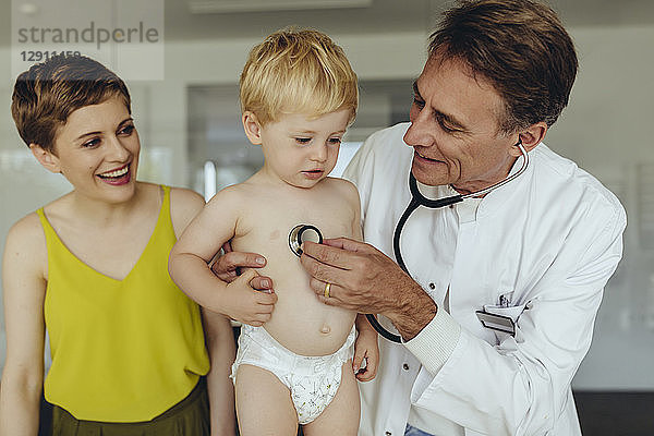 Pediatrician examining toddler with stethoscope  mother standing next to them