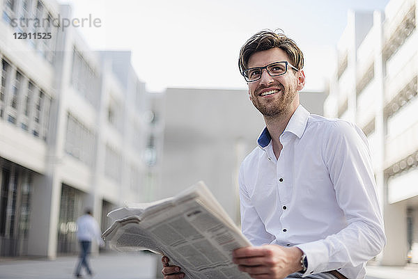 Smiling businessman sitting in the city reading newspaper