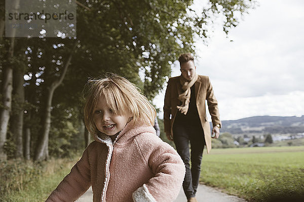 Portrait of blond little girl with father running after her in the background