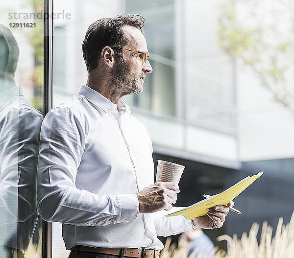 Businessman with papers and coffee to go looking at distance