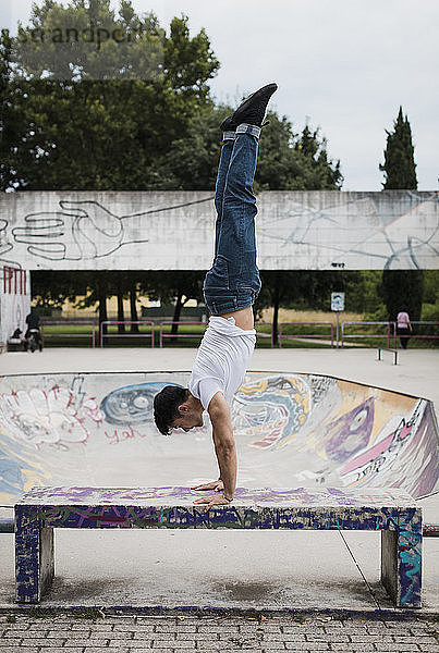 Young man doing a handstand on bench in skatepark