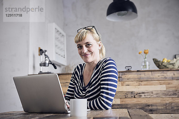 Portrait of smiling woman sitting at table with laptop and coffee mug