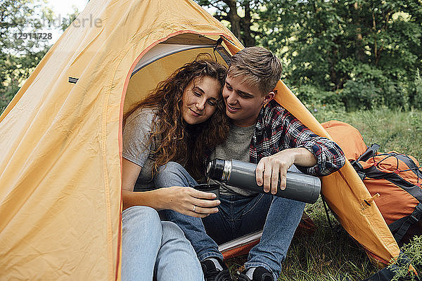 Young couple sitting in tent  drinking tea