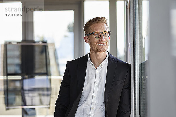 Smiling businessman in office looking out of window