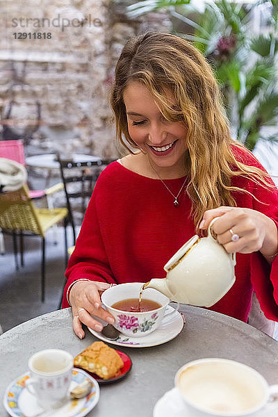 Smiling young woman pouring tea into a cup at pavement cafe