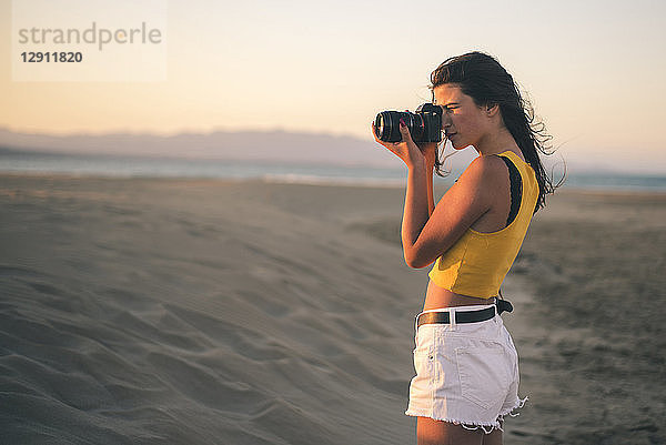 Teenage girl taking photos with camera on the beach at sunset