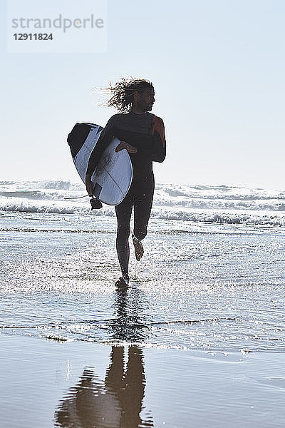 Portugal  Algarve  man running in the water with surfboard