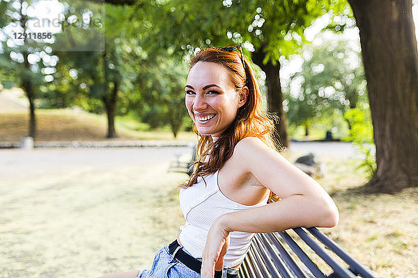 Portrait of laughing redheaded woman sitting on bench in a park