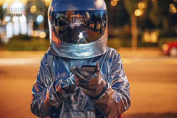 Spaceman on a street in the city at night using smartphone