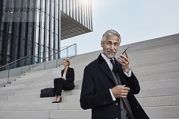 Portrait of businessman on the phone while business woman working on laptop in the background