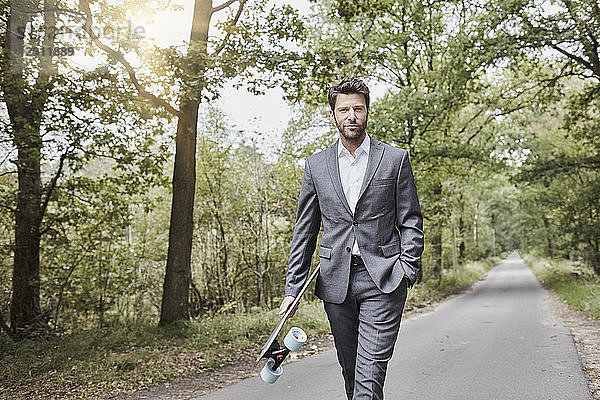 Businessman walking with skateboard on rural road