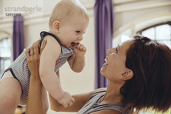 Sporty woman lifting up happy baby in training room