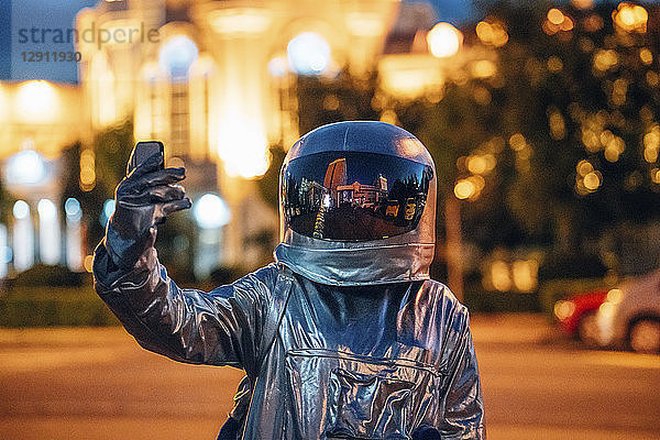 Spaceman on a street in the city at night holding smartphone