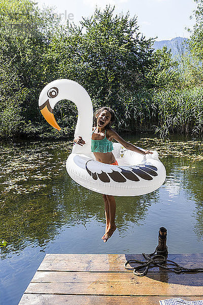 Carefree girl jumping into pond with inflatable pool toy in swan shape