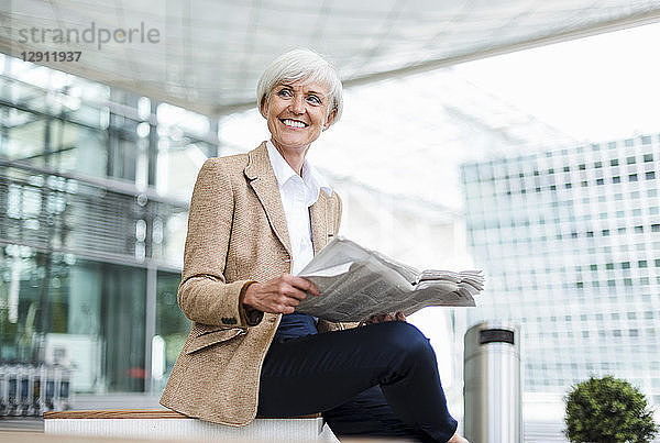 Smiling senior businesswoman sitting in the city with newspaper