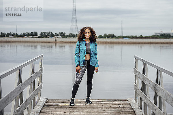Young athletic woman standing on jetty at the riverside