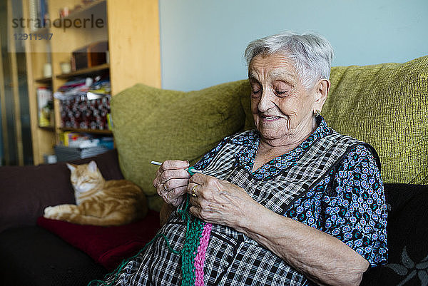 Portrait of crocheting senior woman sitting on couch besides her sleeping cats