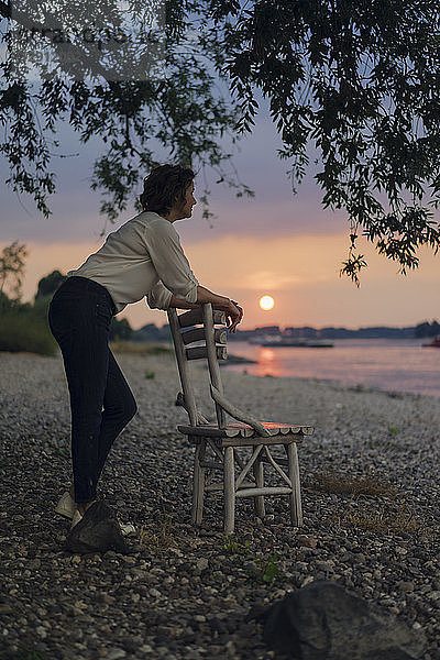 Woman leaning on a chair at the river  watching sunset