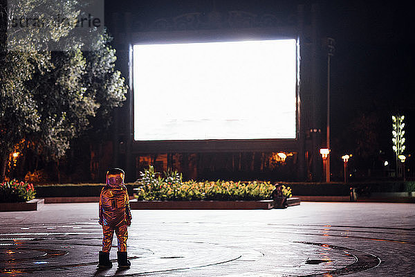 Spaceman on a square at night attracted by shining projection screen