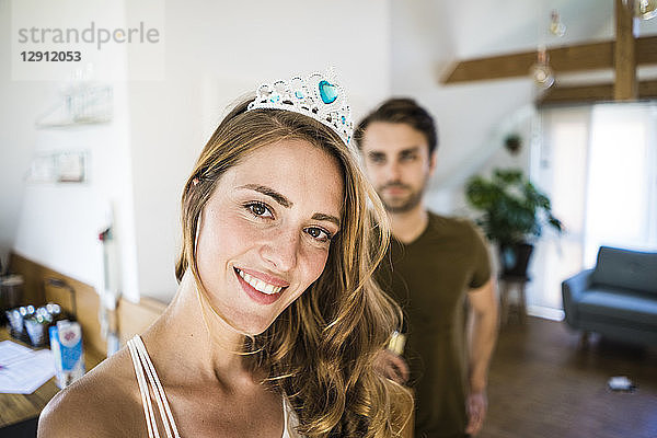 Portrait of smiling woman wearing tiara at home with man in background