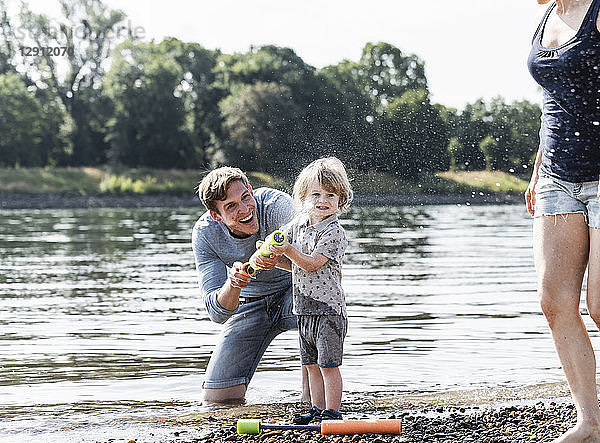 Father and son having fun at the riverside  playing with a water gun