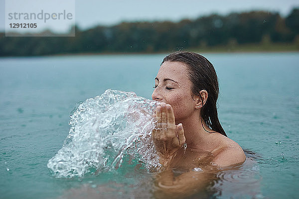 Portrait of young woman bathing in lake splashing with water