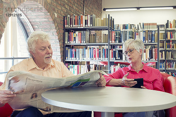 Senior couple with newspaper and e-book in a city library