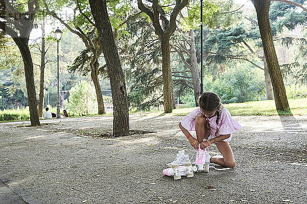 Little girl tying pink roller skates in a park