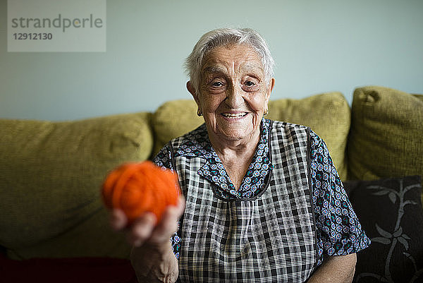 Portrait of smiling senior woman with ball of wool sitting on the couch at home