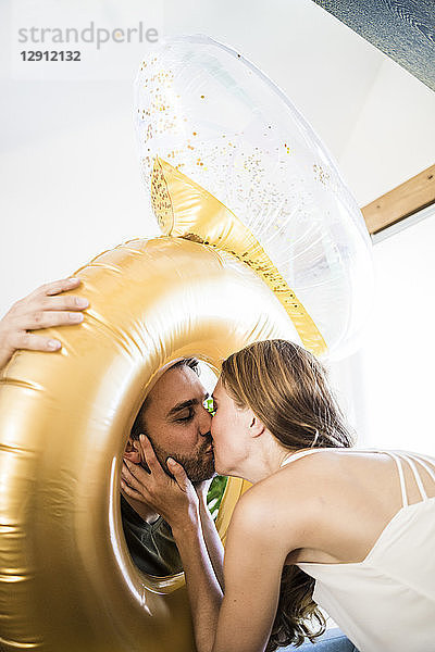 Affectionate couple kissing through large inflatble ring