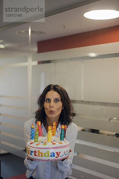 Businesswoman holding birthday cake  blowing out candles