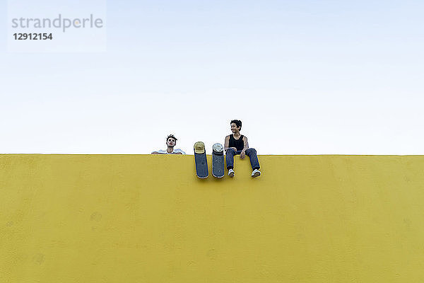 Two young men with skateboards at a high yellow wall