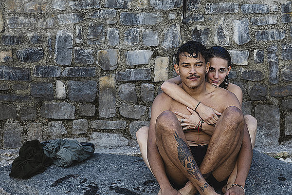 Portrait of affectionate young couple in swimwear sitting at a stone wall