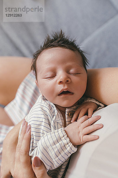 Portrait of newborn baby with closed eyes being held by mother