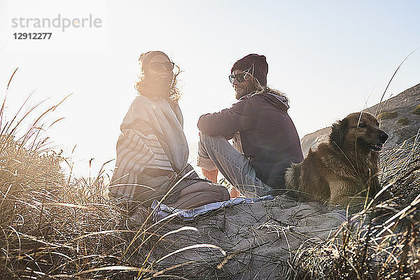 Portugal  Algarve  couple with dog sitting on the beach at sunset