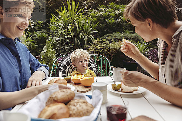 Two happy mothers at breakfast table outdoors with their child