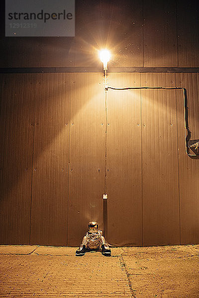 Spaceman sitting under lamp at a wall at night