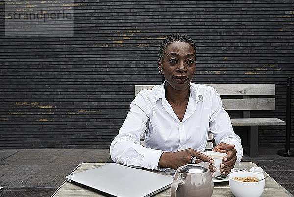 Portrait of businesswoman sitting on terrace of a coffee shop drinking tea