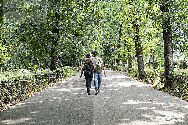 Back view of young gay couple with backpacks walking on a road