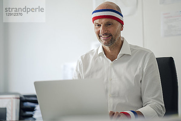Businessman sitting in office  wearing sweat bands  using laptop